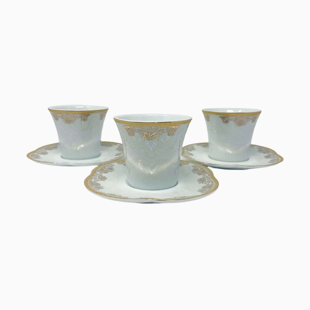 Set of three white cups with gold detailing on saucers against a white background