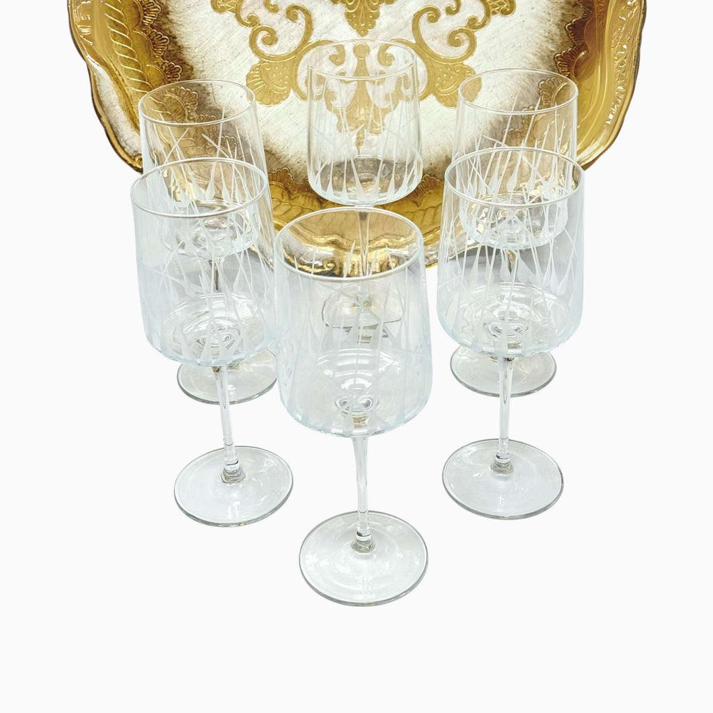 Set of six clear wine glasses on a white background with a decorative gold tray.