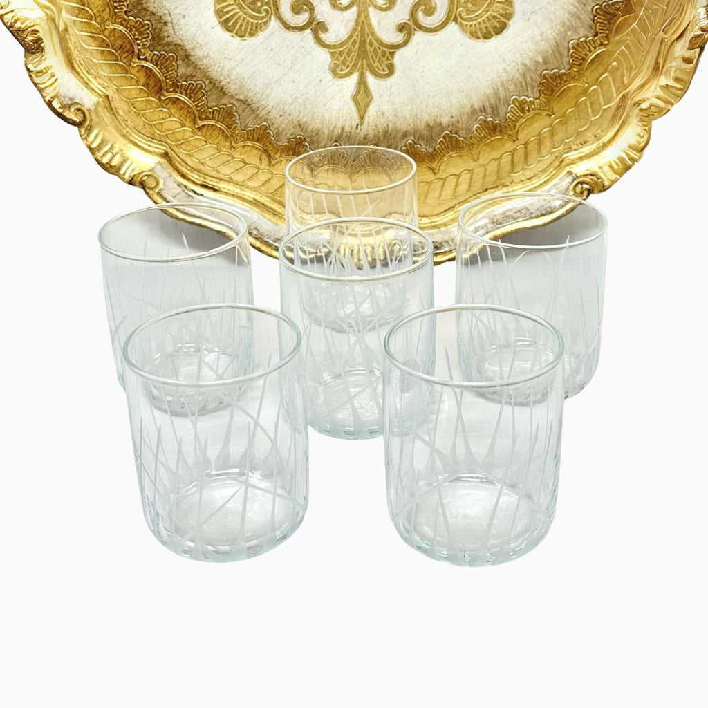 Set of six clear glass tumblers with a gold decorative tray on a white background