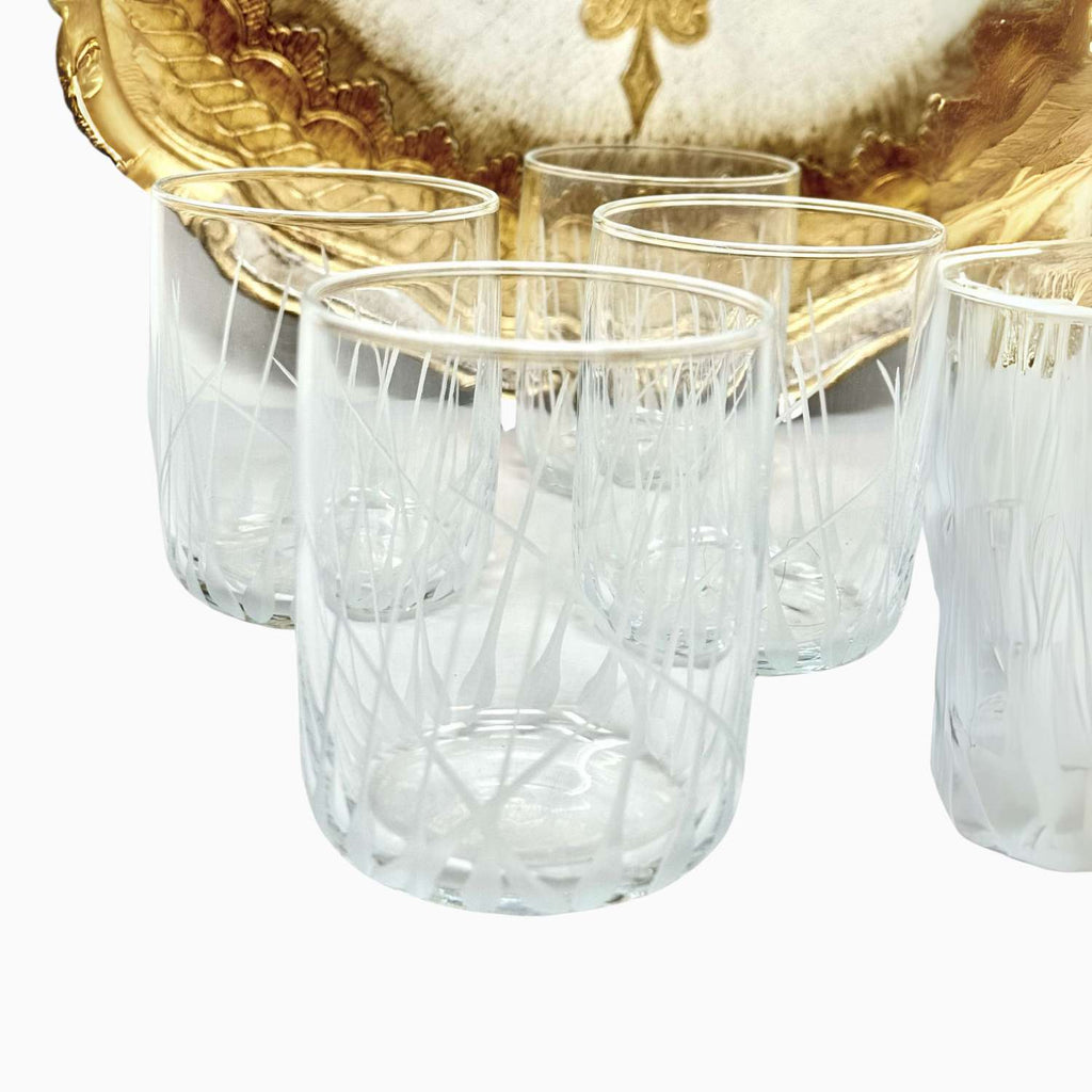 Set of clear glass tumblers with a gold decorative plate in the background