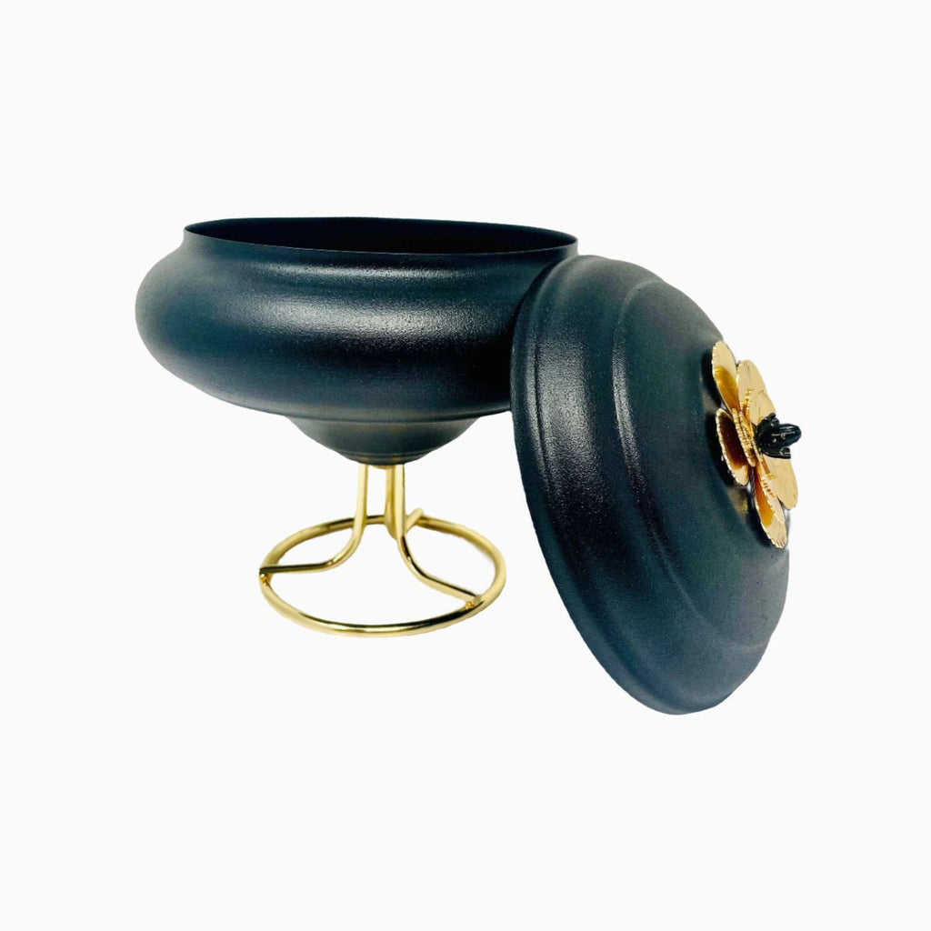 Black decorative bowl with gold base and floral design on a white background