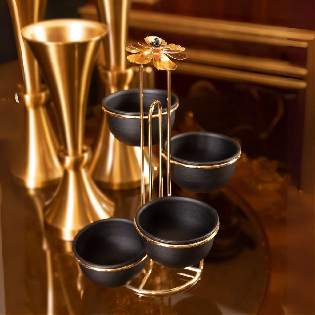 Decorative black and gold vase with a floral top on a reflective surface.