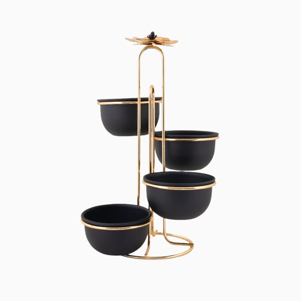 A brass tiered serving stand with four black bowls, topped with a decorative element, used for serving snacks or as a decorative piece.