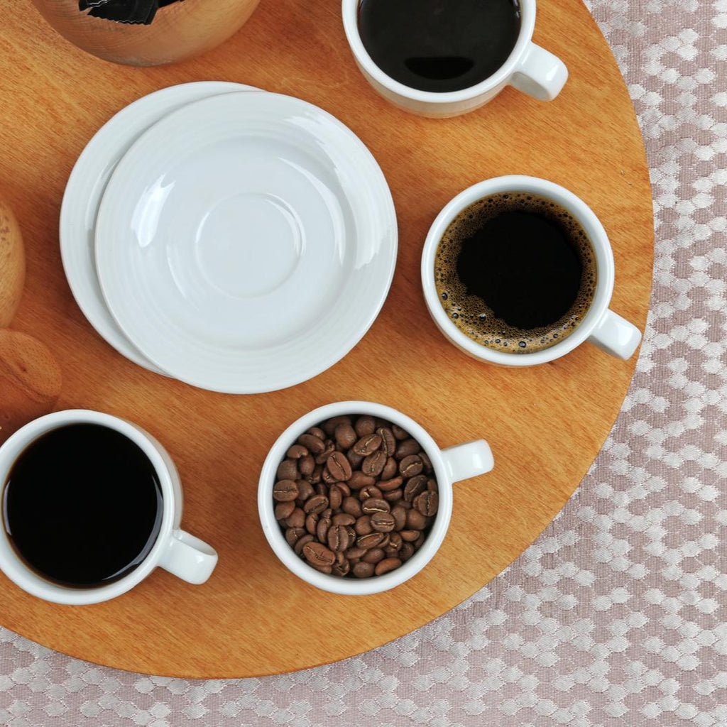 Wooden tray with coffee cups and a bowl of coffee beans on a patterned surface.