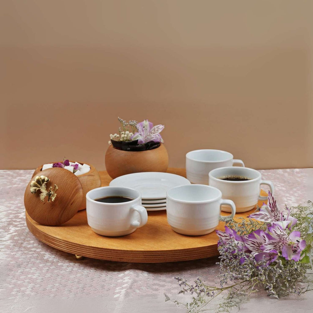 Tea set with cups and a wooden tray on a table with flowers and a plant.