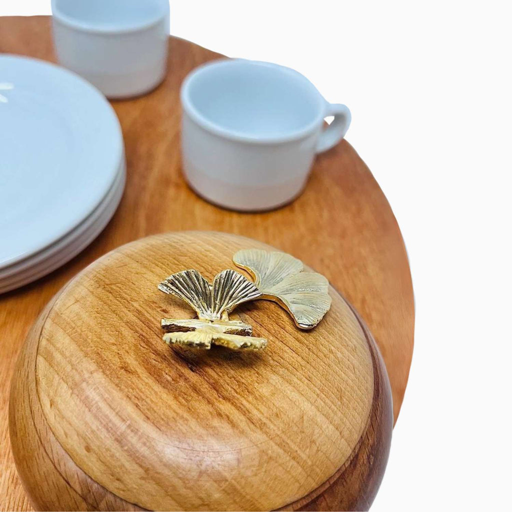 Wooden container with a gold leaf design on a wooden surface with white cups and plates.