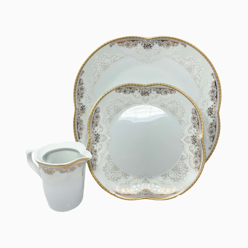 Dinnerware set with ornate plates and a cream pitcher on a white background