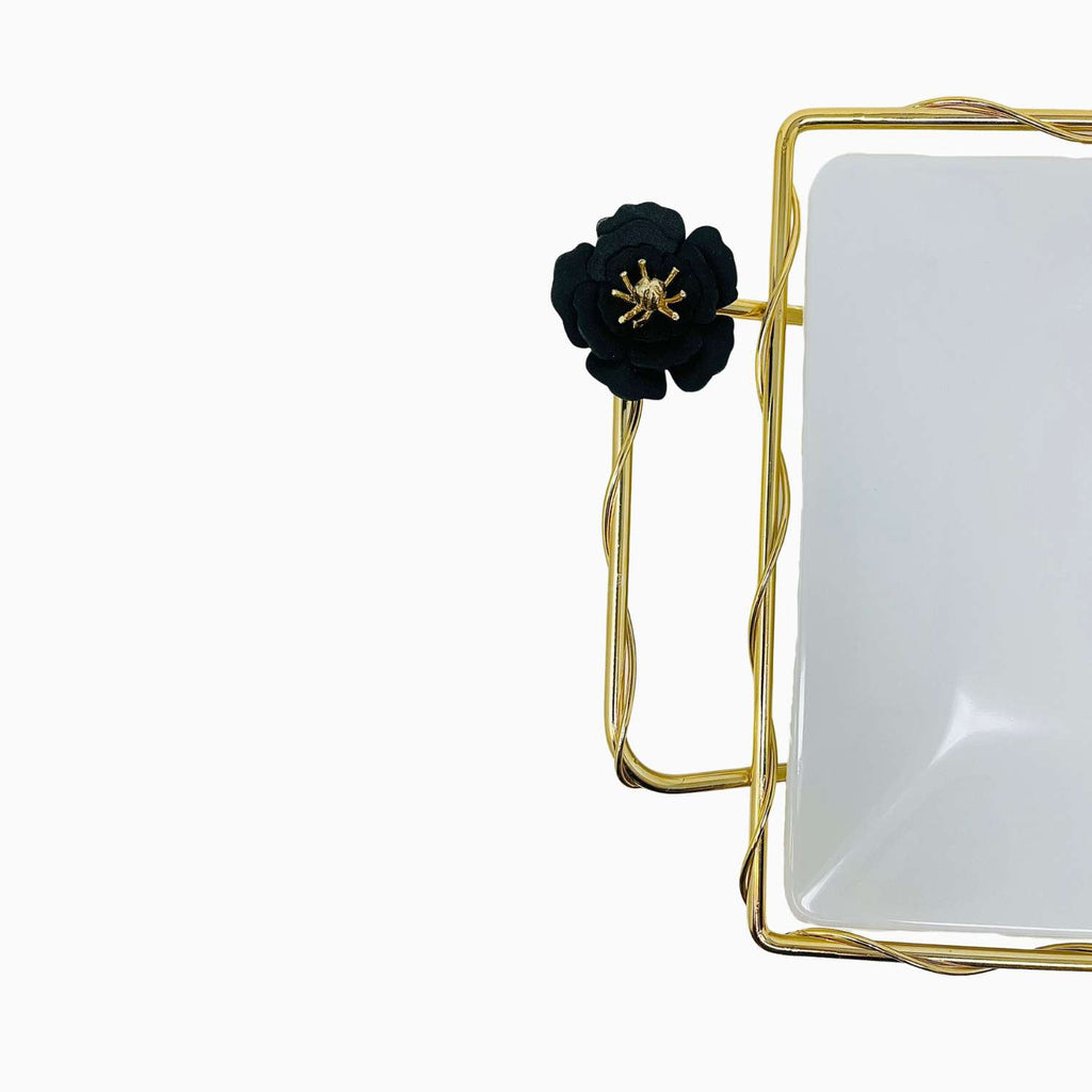 Decorative serving plate with gold frame and black flower on a white background