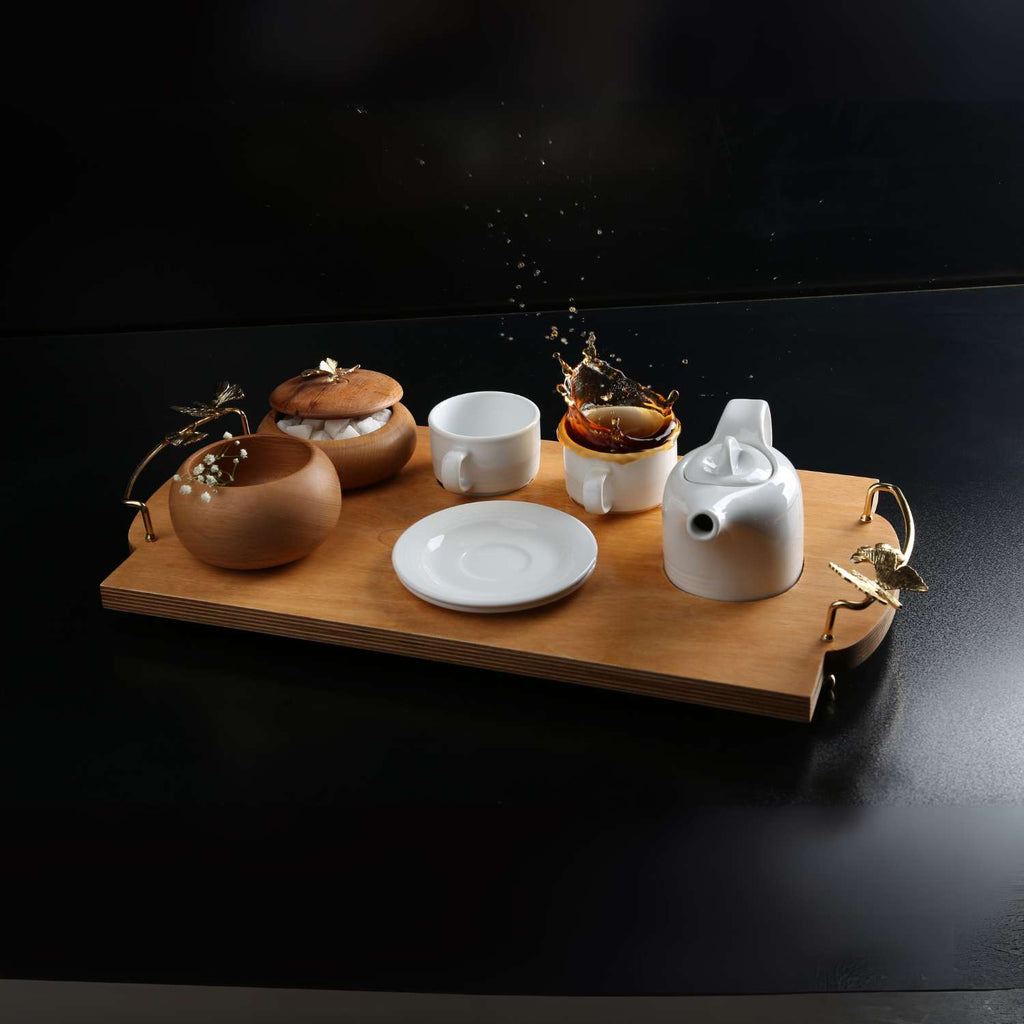 Tea set with ceramic teapot, cups, and a wooden tray on a dark background